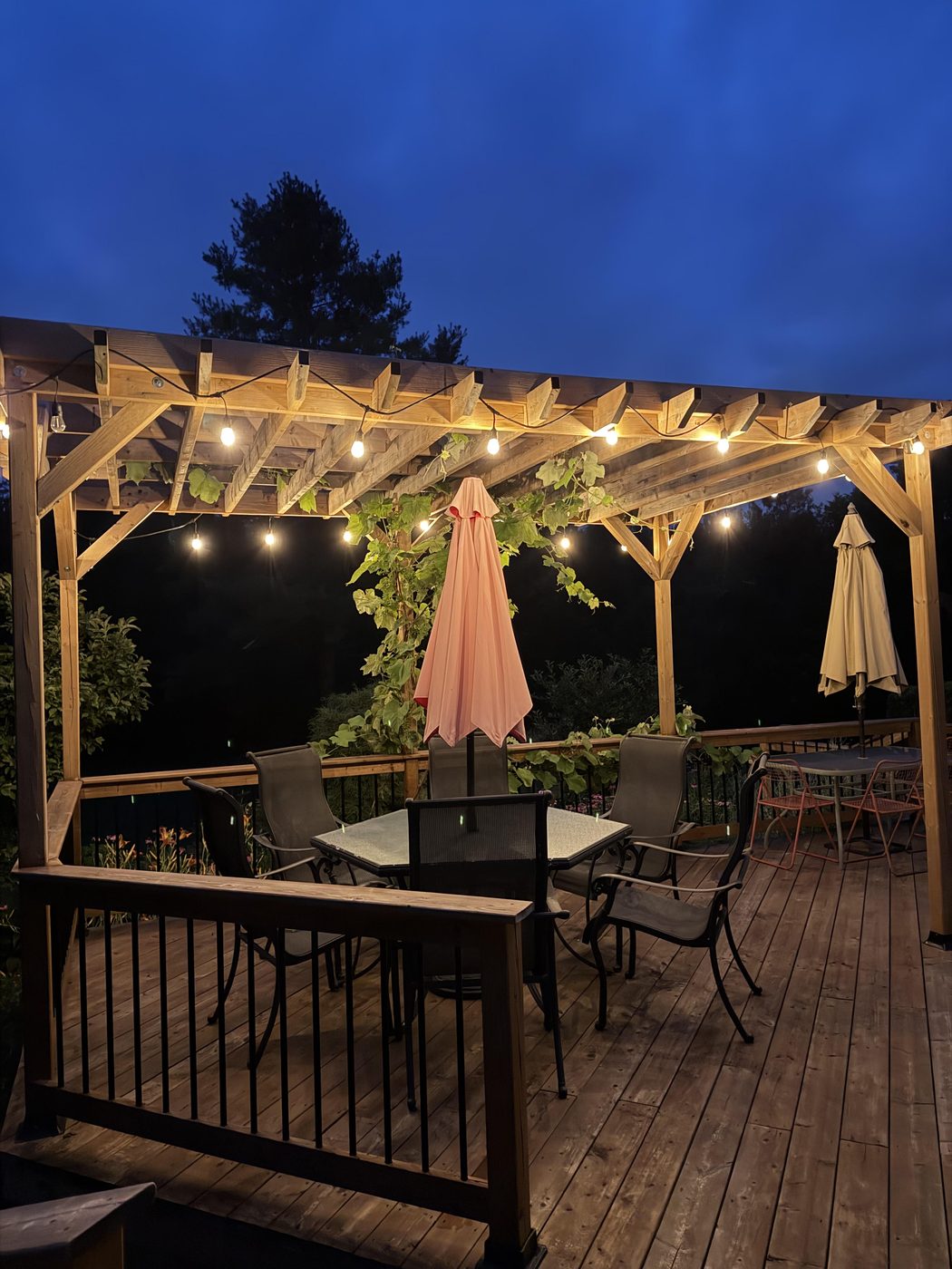 String lights along the pergola beams, with a second table further along the deck